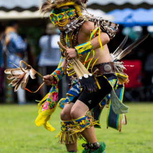 performers wearing vibrant traditional attire perform a dance at a 4th of July powwow, while spectators watch.