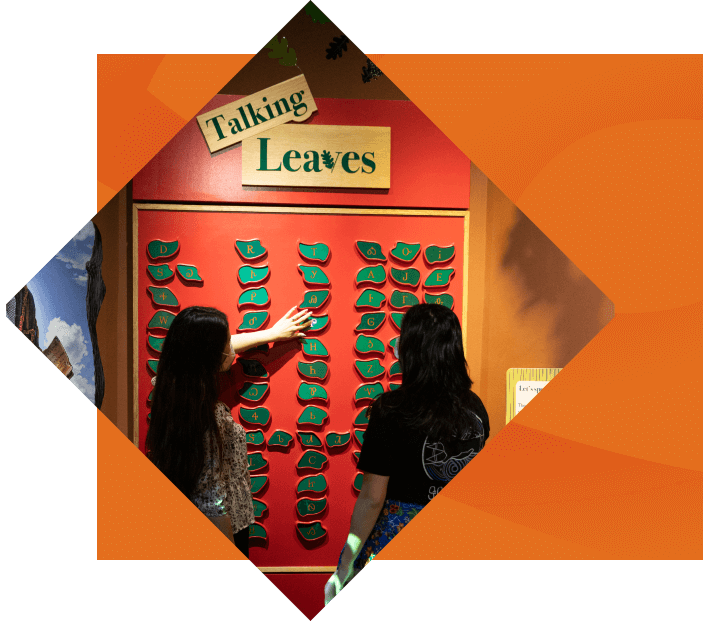 Two people interacting with a red interactive display titled "talking leaves," featuring numerous green handsets in a museum setting, surrounded by a stylized orange frame.